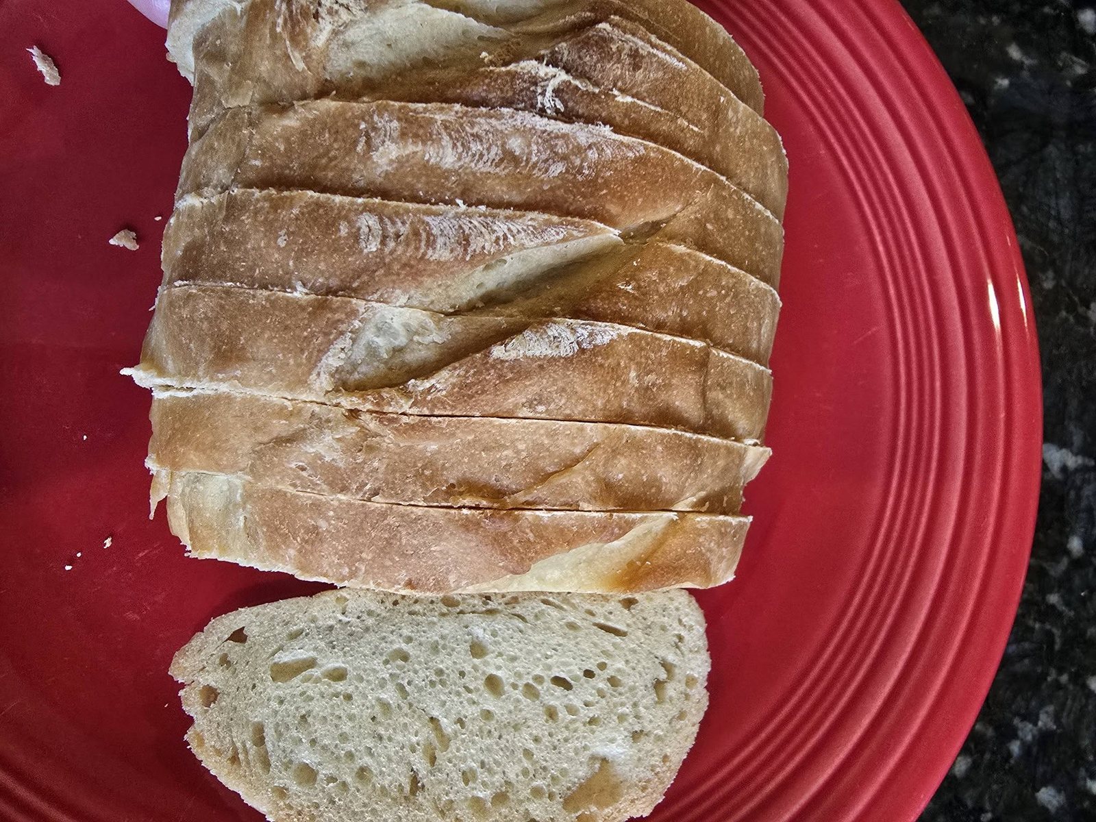 A sourdough loaf sliced on a red plate, showing an open airy crumb