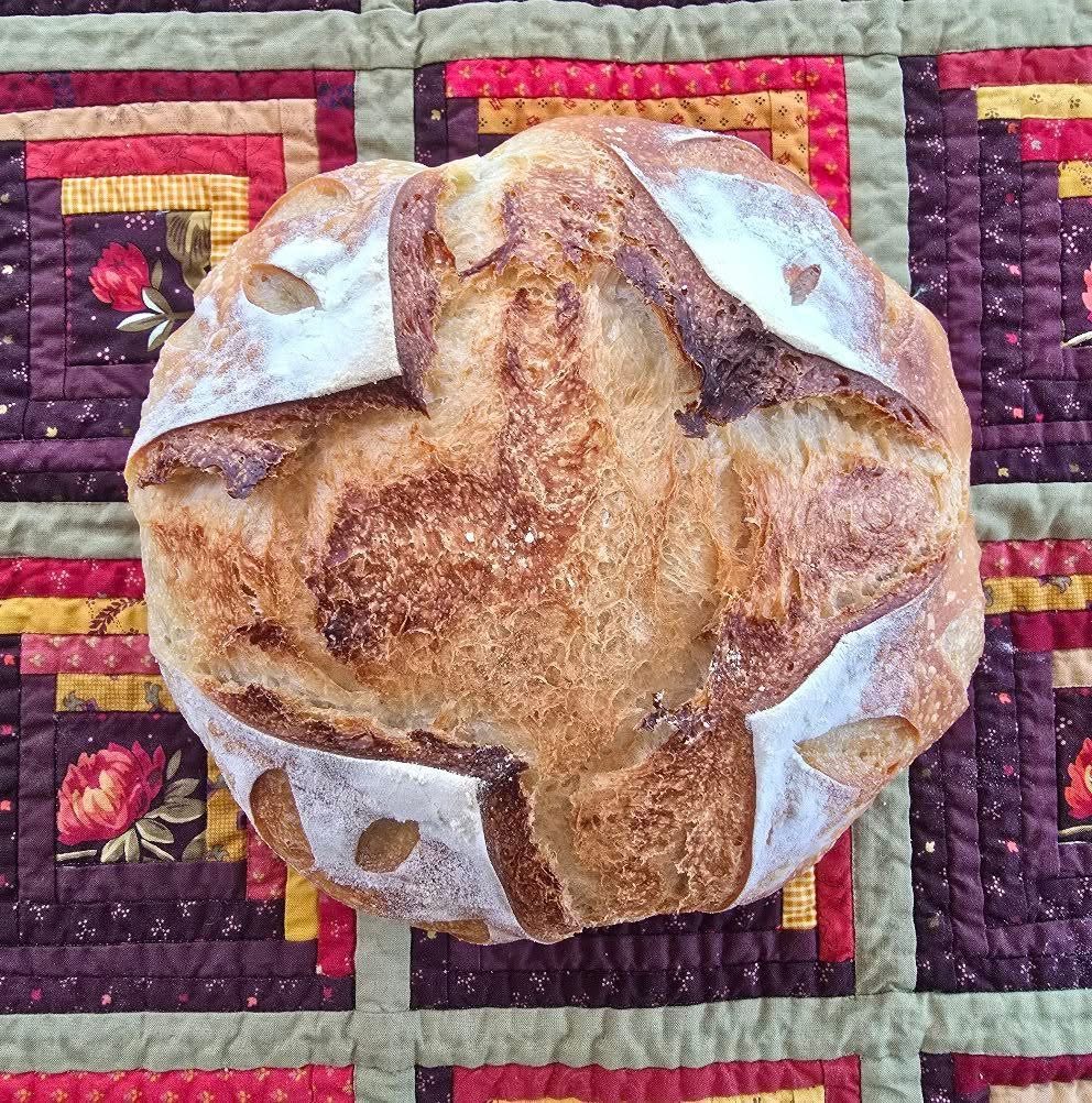 A round hand scored sourdough loaf resting on a patchwork quilt